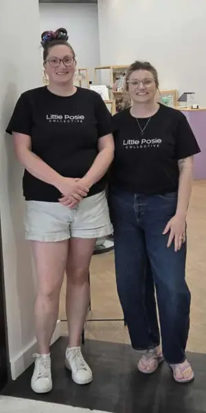 Candice and Brooke smiling and standing at the front of their retail store in black t-shirts with the store name Little Posie Collective.